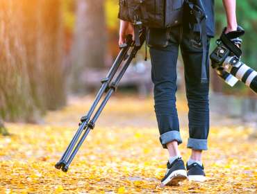 Professional photographer with camera and tripod in autumn.