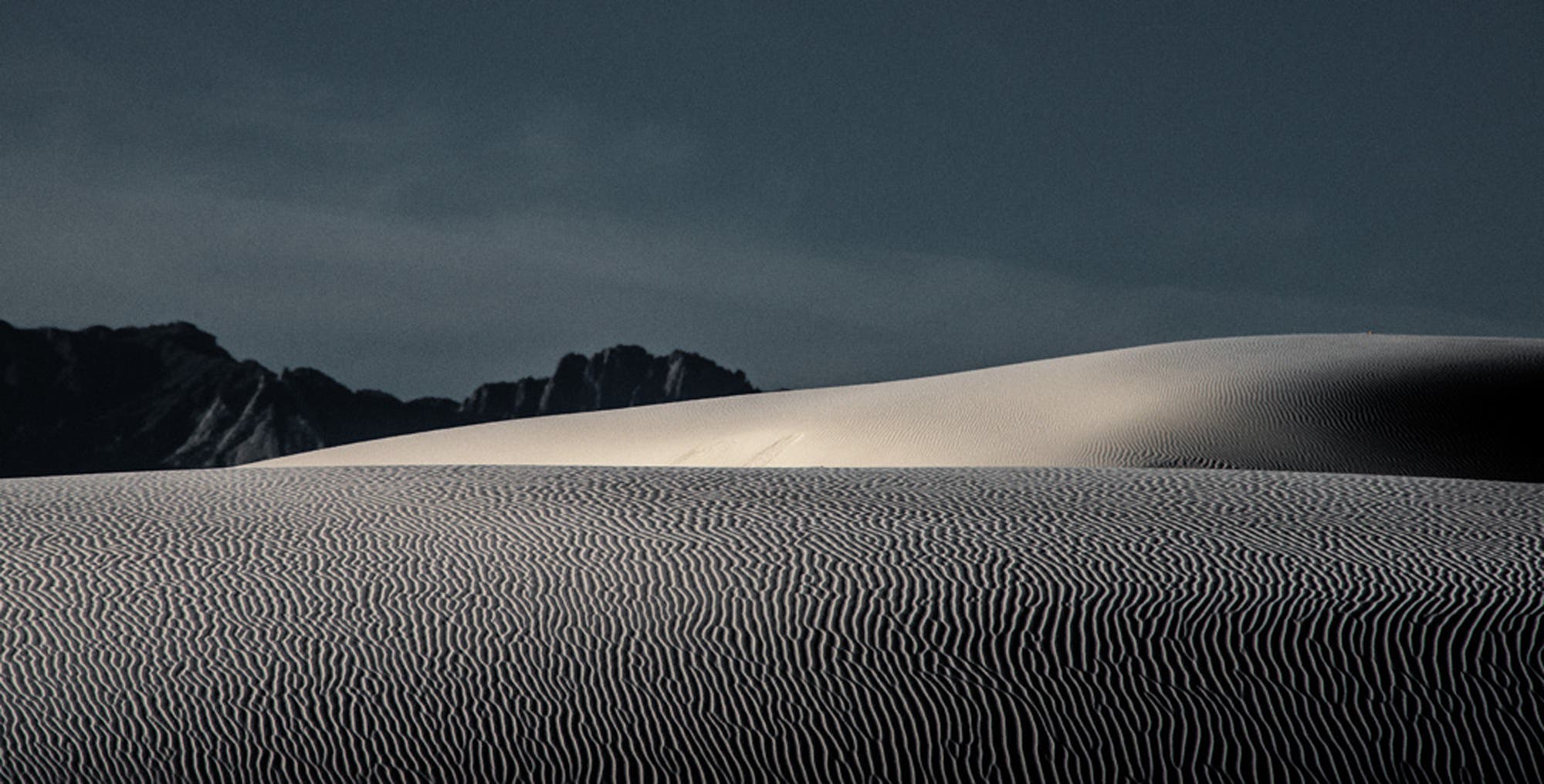 The low-angled light of the late afternoon sun casts the kind of shadows that bring out surface texture, as on these gypsum dunes in White Sands National Monument. I watched as the clouds let the sun through in some places more than in others and took the shot when the second dune was highlighted while the closest dune was less brilliantly lit. I metered the brighter dune to maximize the texture on the first dune. Taken at 300mm with my 28-300 zoom lens at f/16 for sharpness.