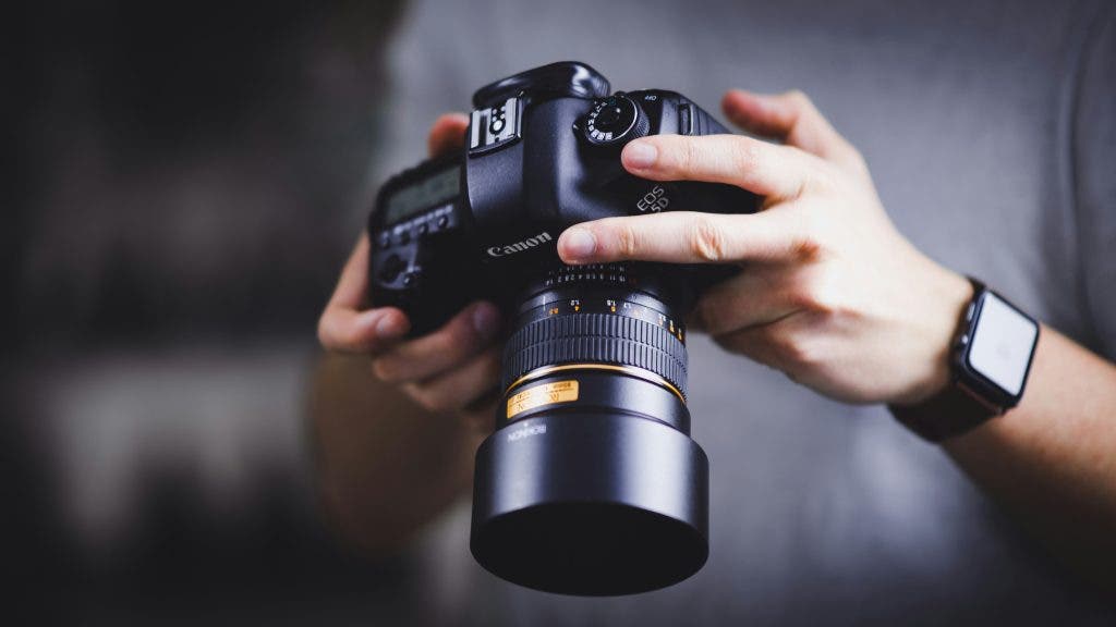 Man wearing a smart watch holds a camera with a medium lens