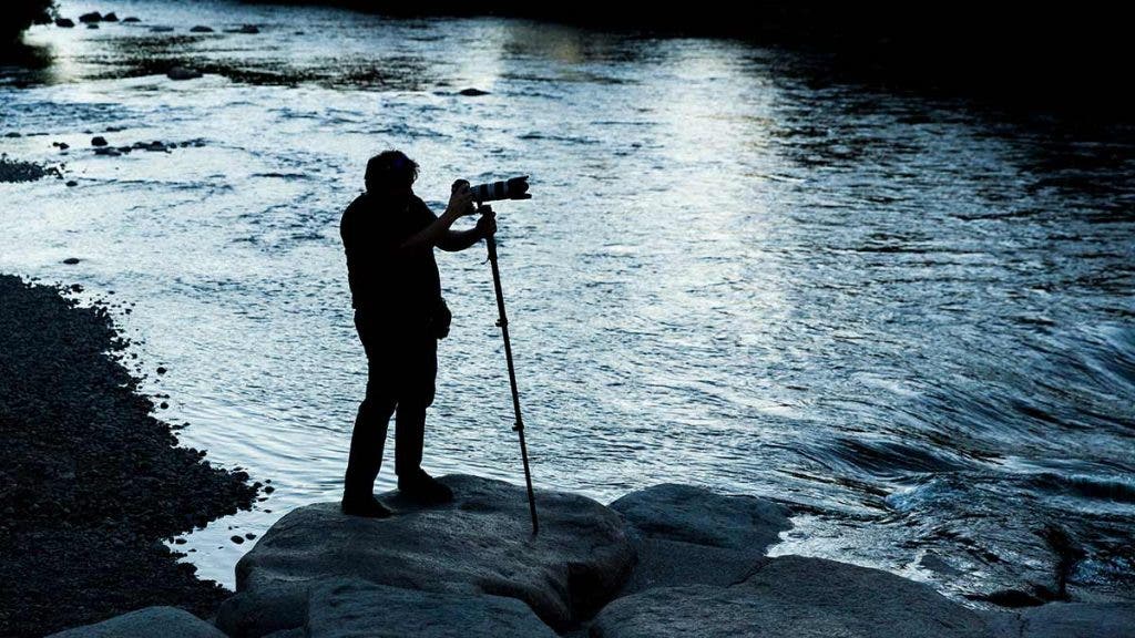 photographer with camera monopod doing landscape photography on lake