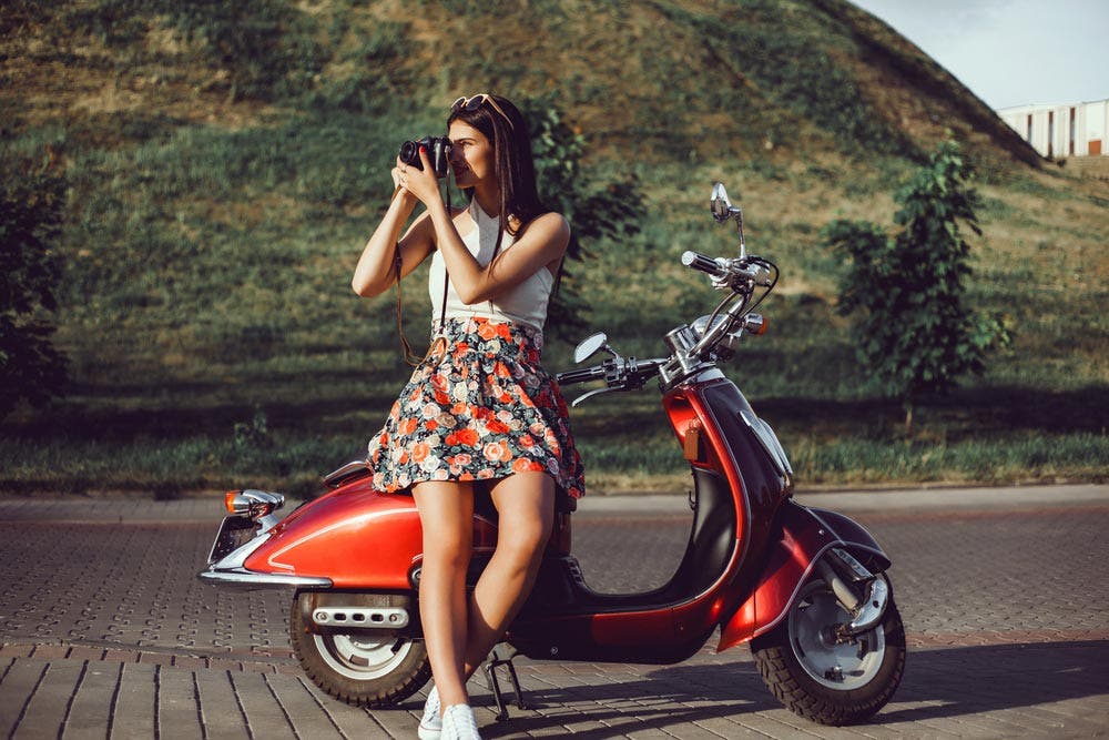 woman sitting on a vespa while taking pictures