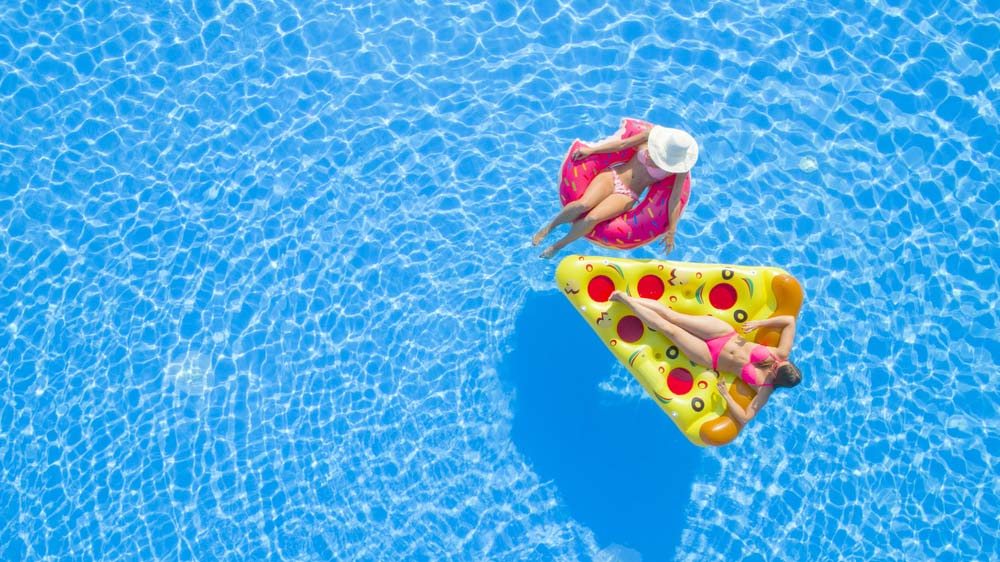 two women lying on pool floaties in swimming pool