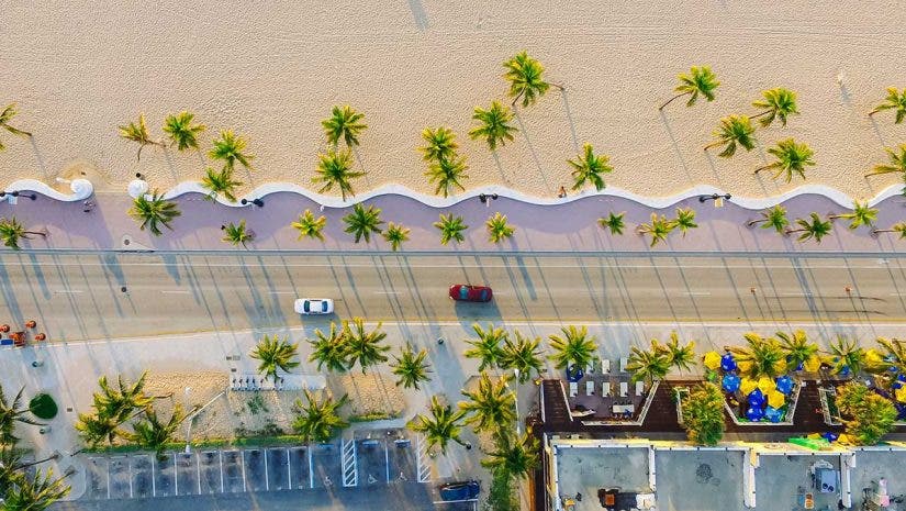 drone photography of beach boardwalk, cars, and palm trees