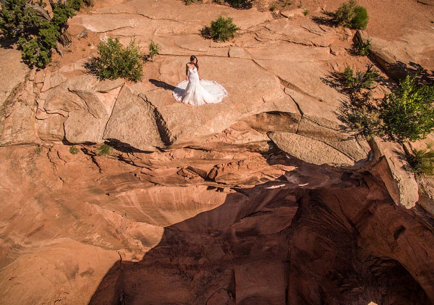drone aerial shot of bride in white wedding dress standing on a cliff