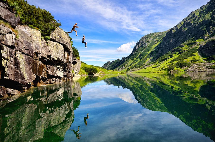 couple jumping into a lake surrounded by green mountains