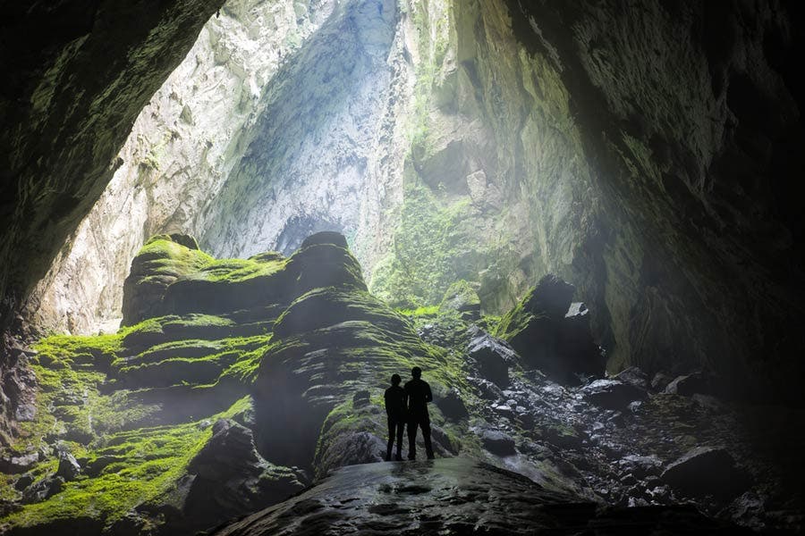 two people standing in a moss covered cave