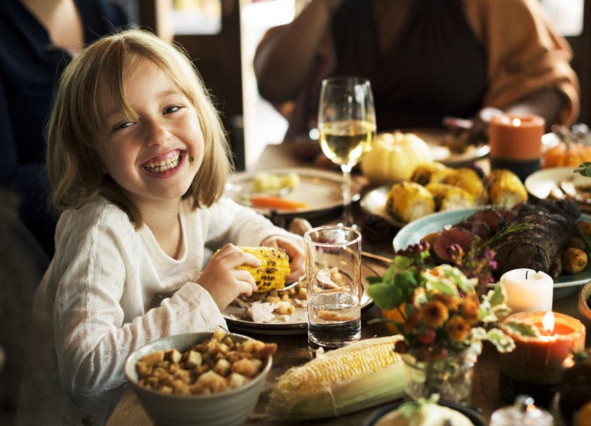 little girl smiling while eating at thanksgiving celebration with family