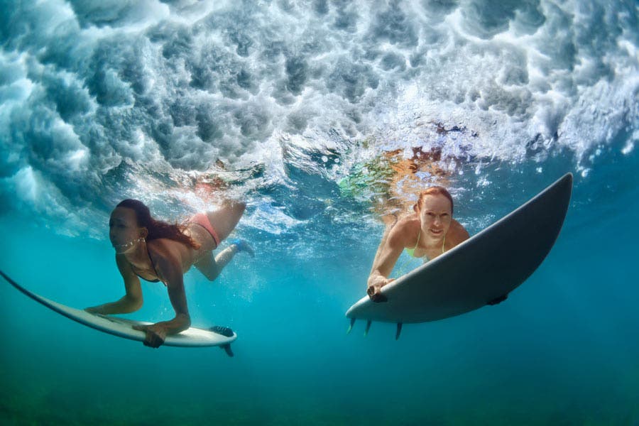 two women surfers diving underwater with surfboards