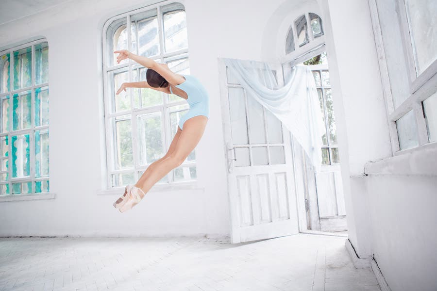 Faceless portrait of little girl ballerina in blue leotard floating in a white room