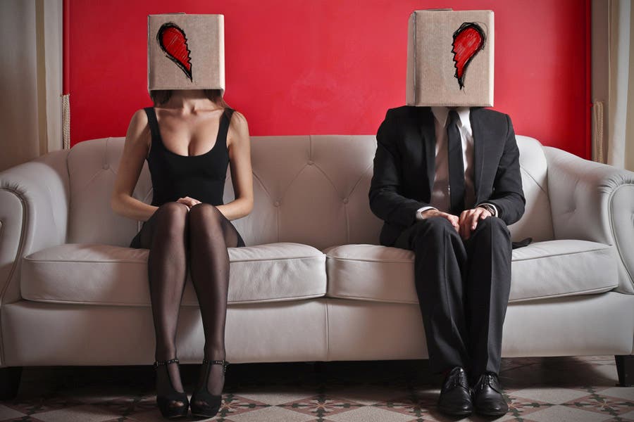 Faceless portrait of couple sitting on couch with broken heart boxes over their heads