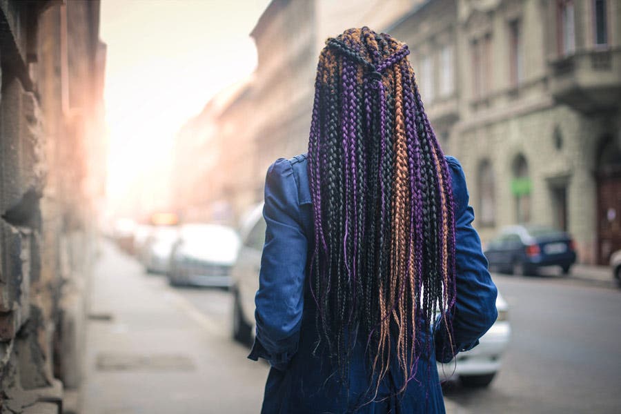 Faceless portrait of chic woman with colorful braids walking down the street