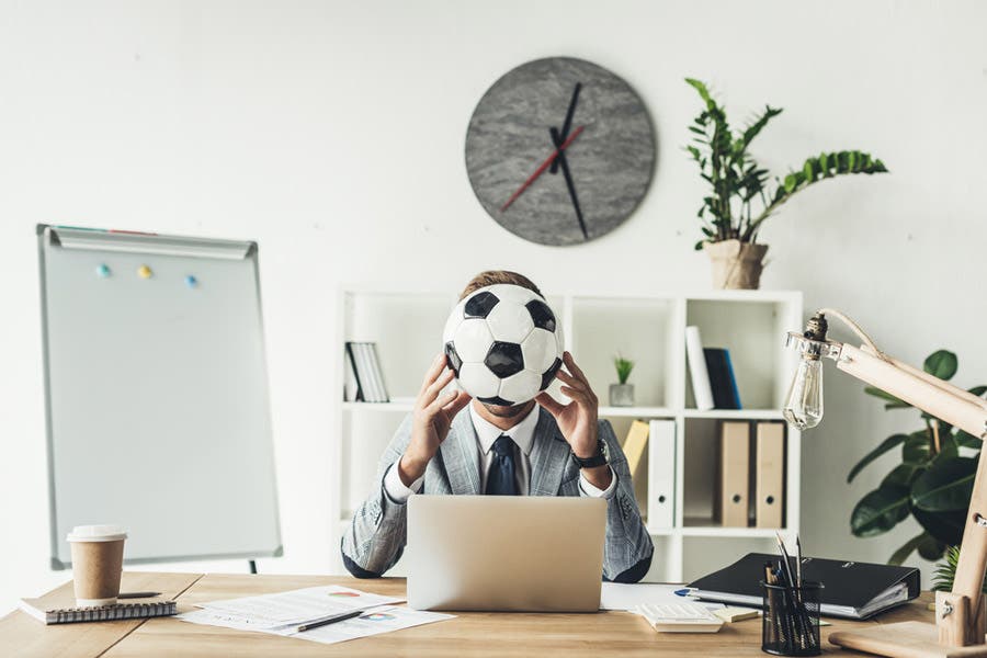 Faceless portrait of man in the office holding soccer ball over his face