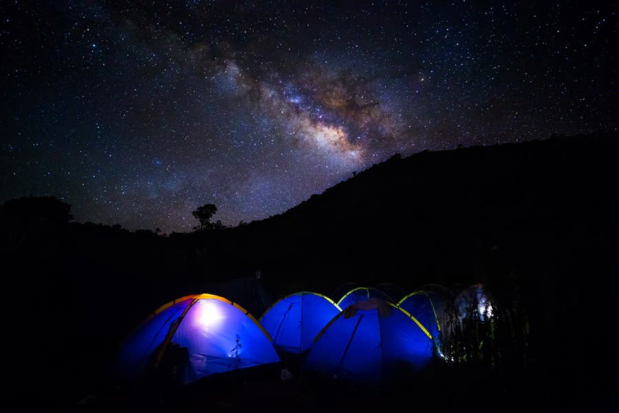 starry night sky with glowing purple tents astrophotography