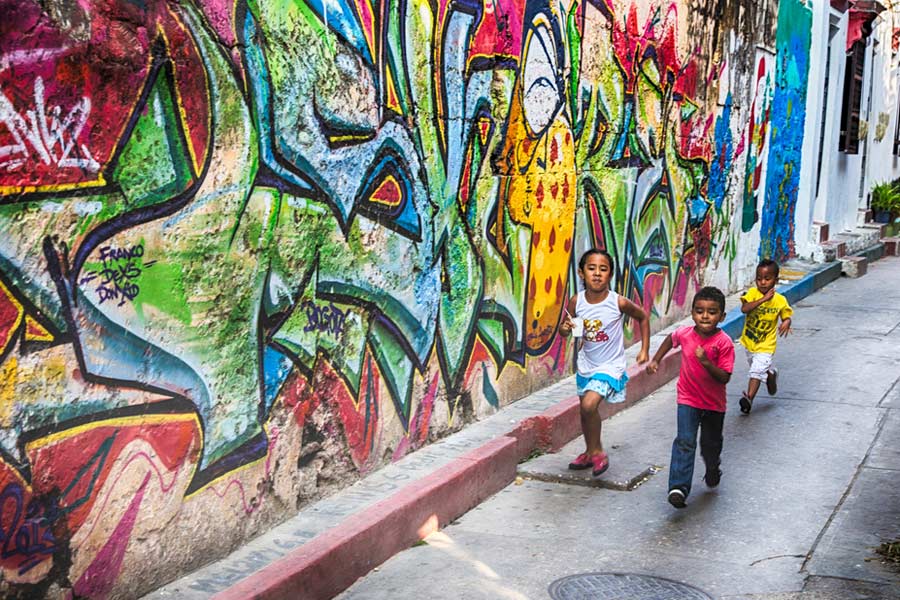 local children running along graffiti art in a street in Colombia
