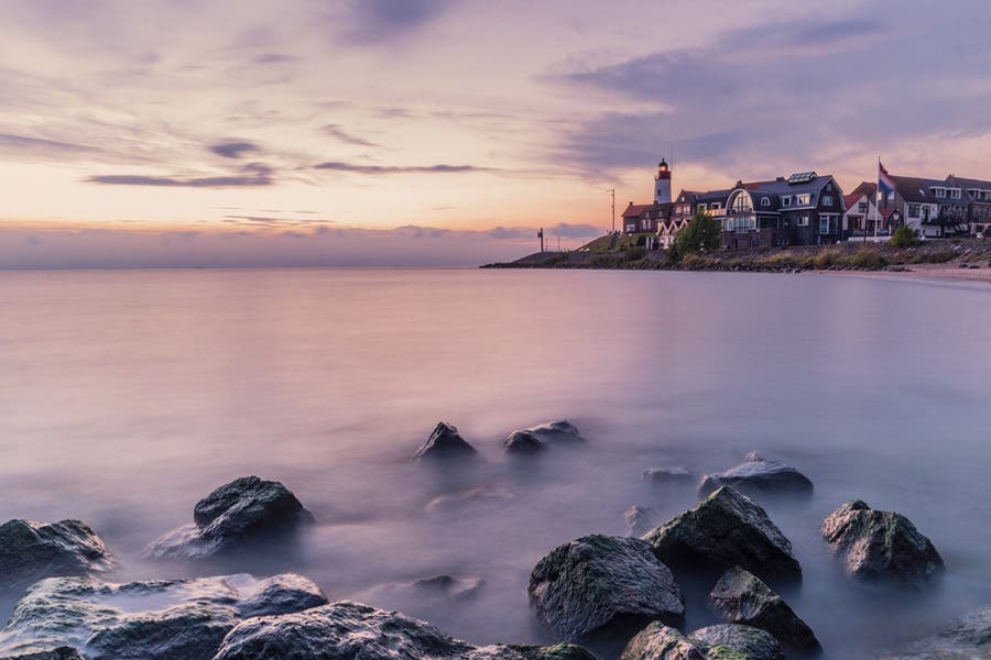 faraway lighthouse surrounded by houses with rocks in the foreground