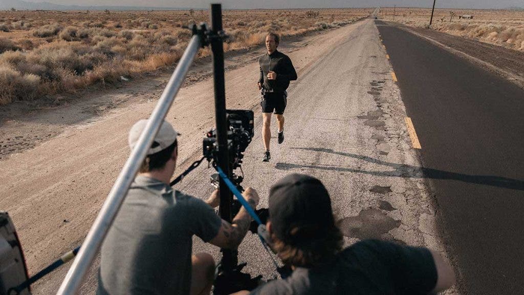 cinematographer with camera filming runner in desert