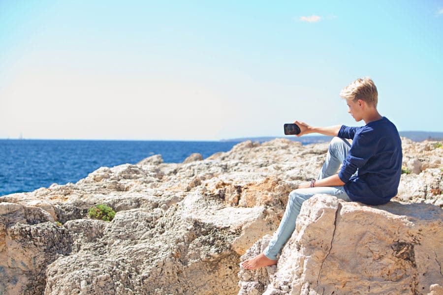 young man taking a photo of the sea with his mobile phone in broad daylight