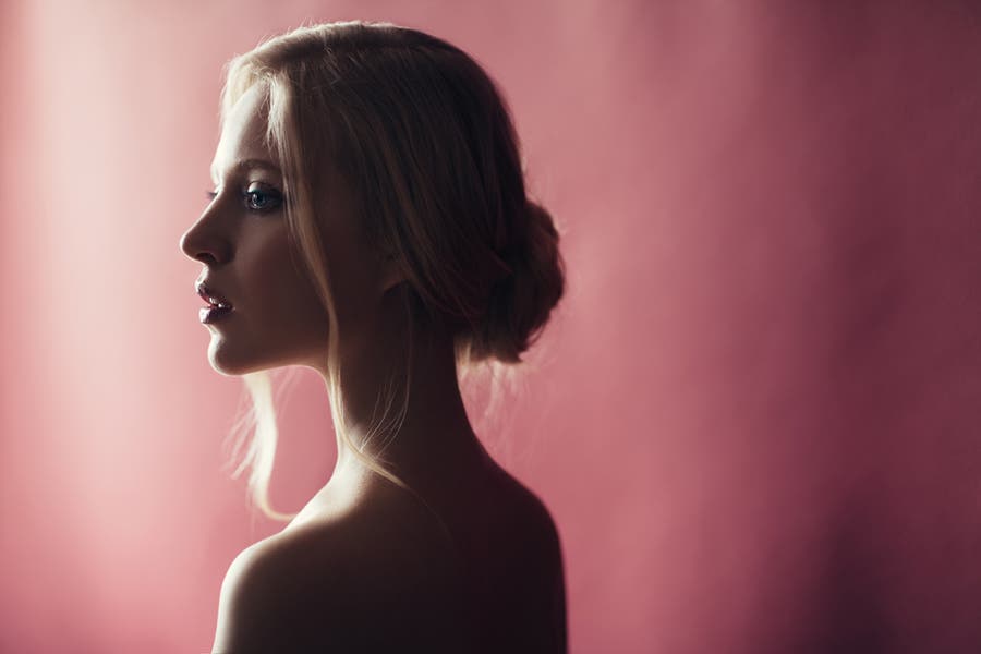 Semi silhouetted side portrait of blonde woman against rose pink background