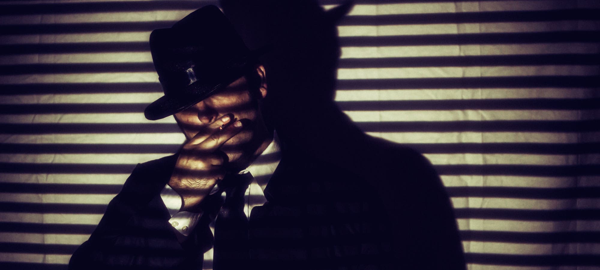 Man smoking behind shadows of blinds