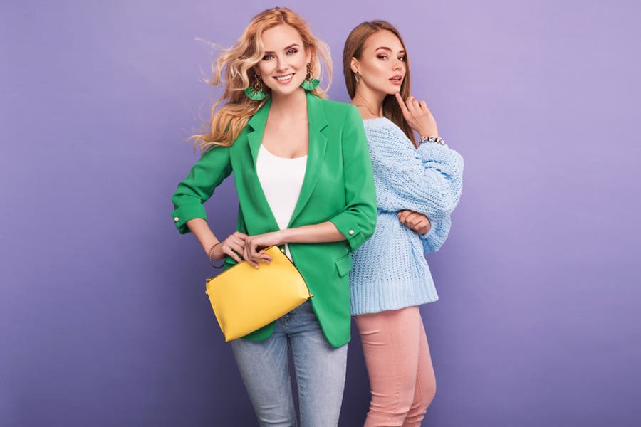 two female models in colorful outfits against purple studio background