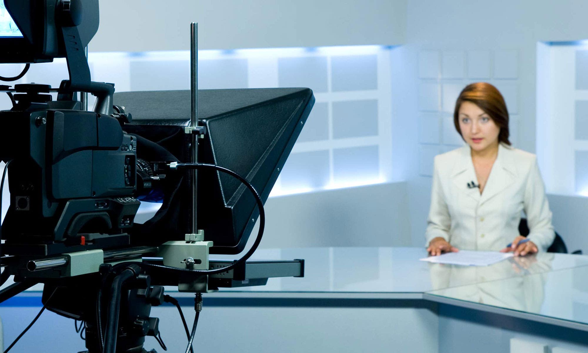 female TV anchor sitting in front of camera and teleprompter