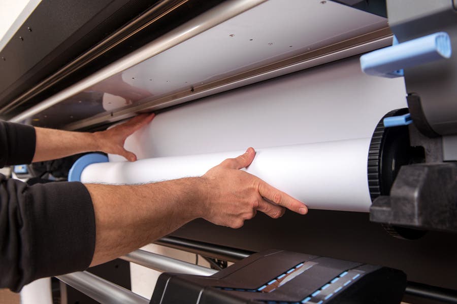 man loading a roll of paper inside a wide format printer