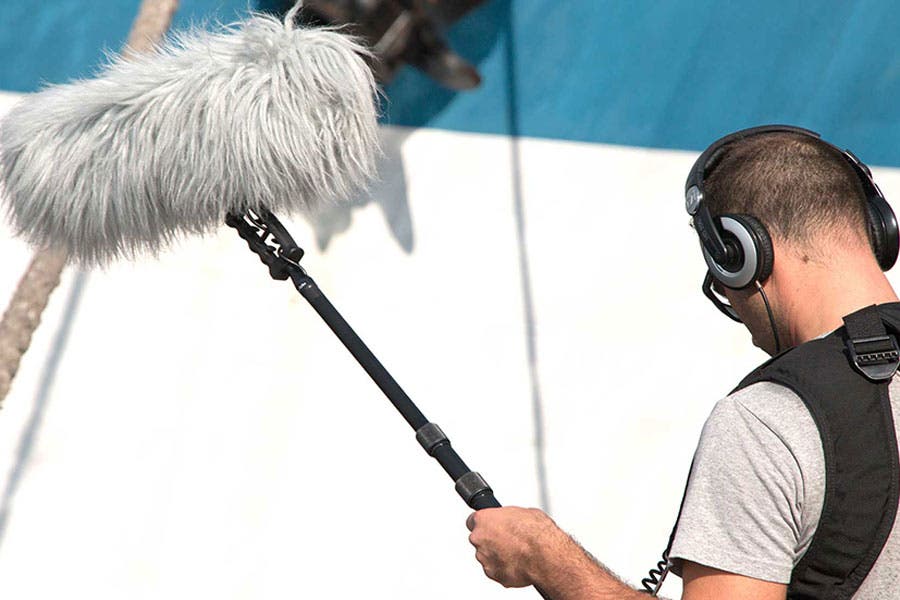 production crew member holding a shotgun mic with a wind muff