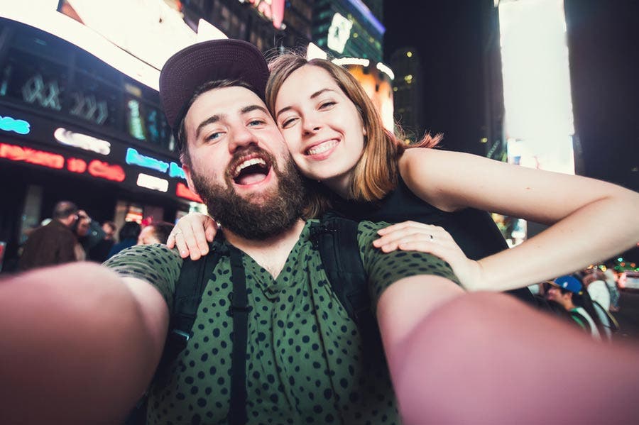 happy couple smiling and posing while taking a selfie in Times Square