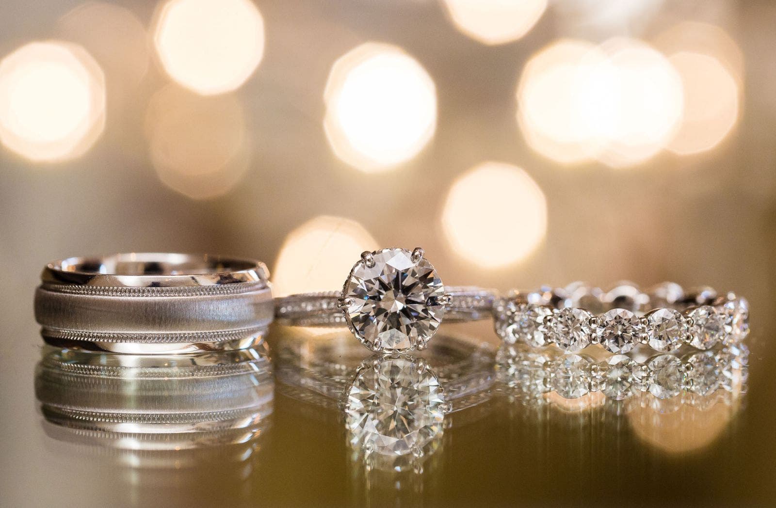 Wedding rings on a reflective surface in front of string lights