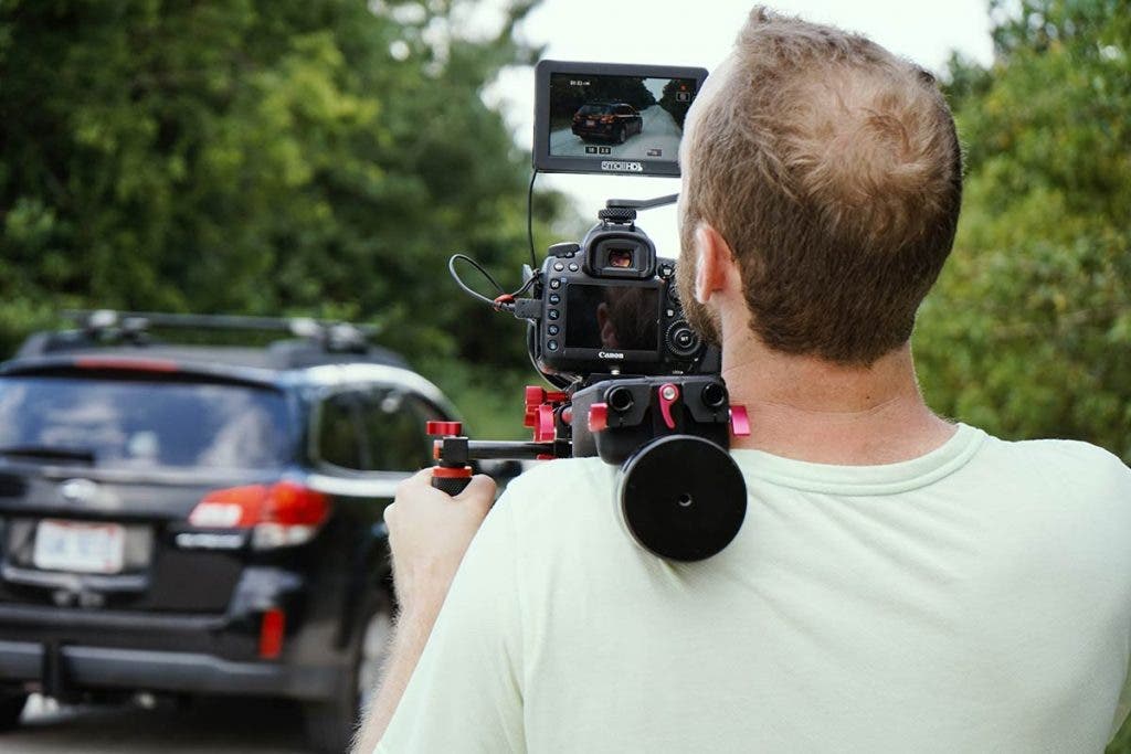 documentary filmmaker with cinema camera filming a car