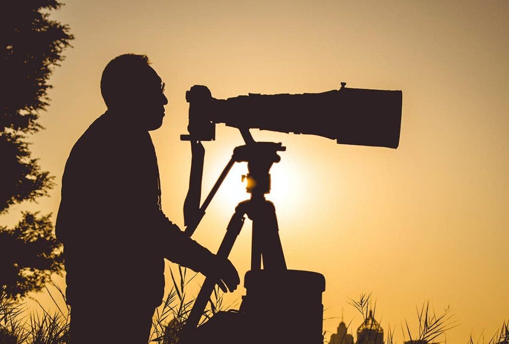 wildlife photographer with telephoto zoom lens on tripod at sunset