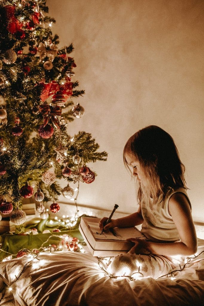 Girl writing list next to Christmas tree