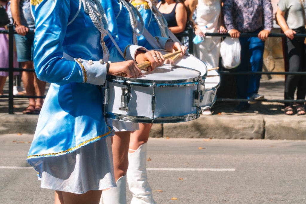 Street performance of festive march of drummers girls in blue costumes on city street. Close-up of female hands drummers are knocking in the drum of their sticks