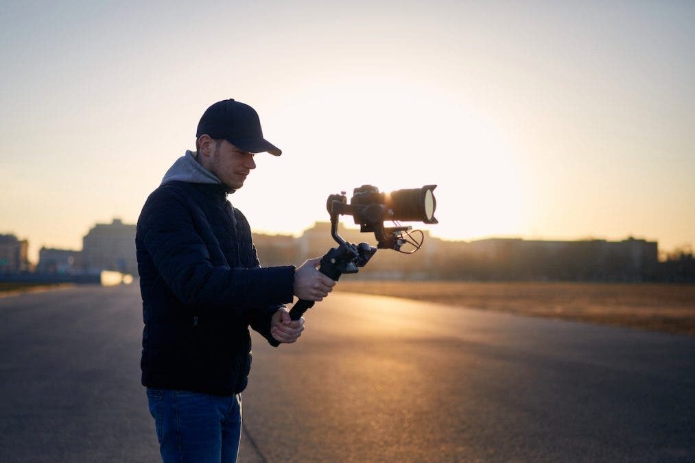Man filming with camera and gimbal against city at sunrise