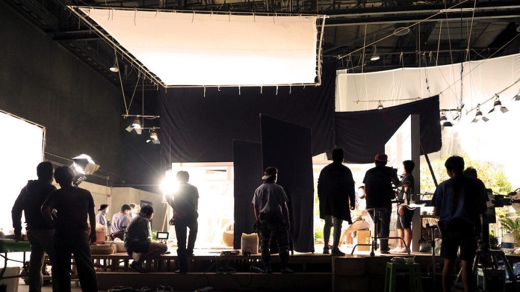 Silhouette of people working in big production studio for shooting or recording movie video by digital camera and lighting set.