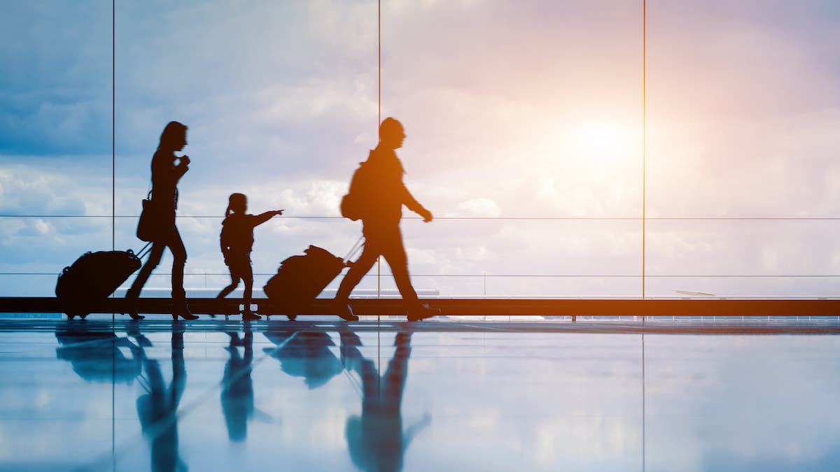 Family at airport travelling with young child and luggage walking to departure gate, girl pointing at airplanes through window, silhouette of people, abstract international air travel concept