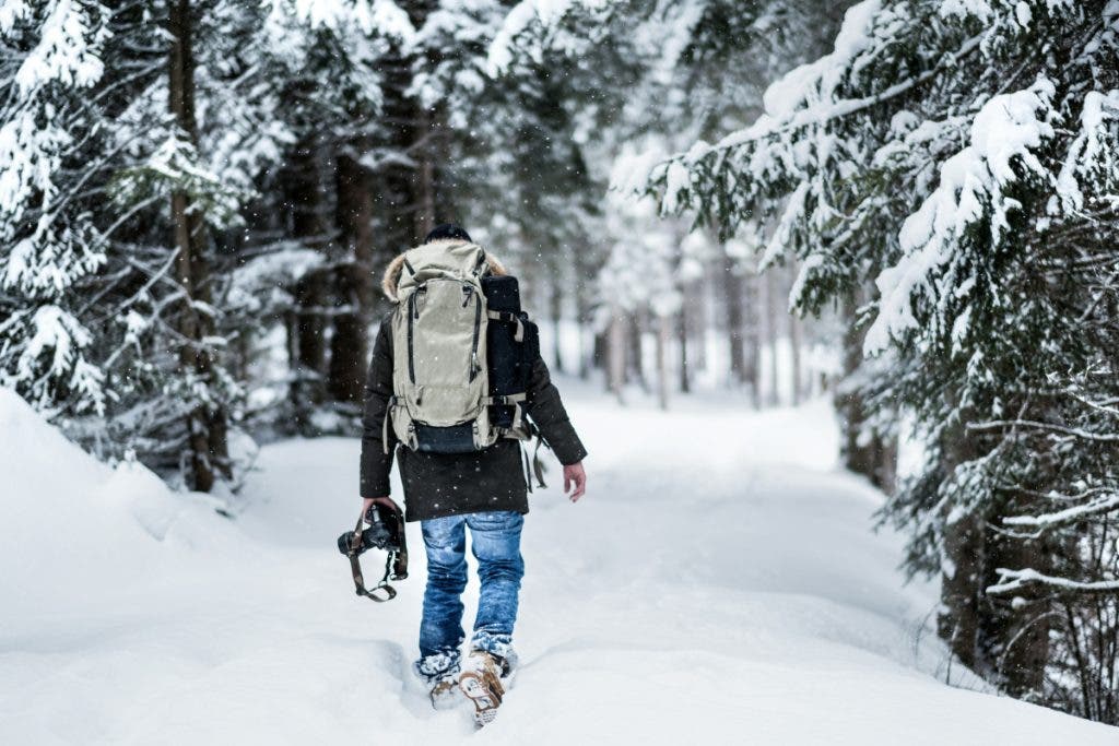 Photographer walks through snow with camera backpack for outdoor photography
