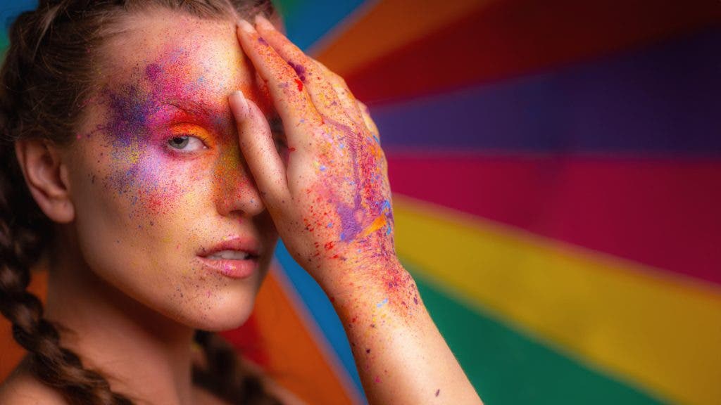 A colorful background reflects the colorful makeup on this female model's face and hands. She has one hand covering her eye. This was certainly the best camera for portraits that day.