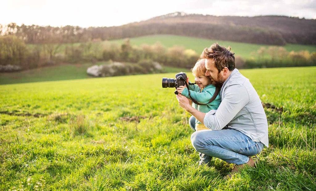 A father and his toddler son with a camera outside in spring nature.