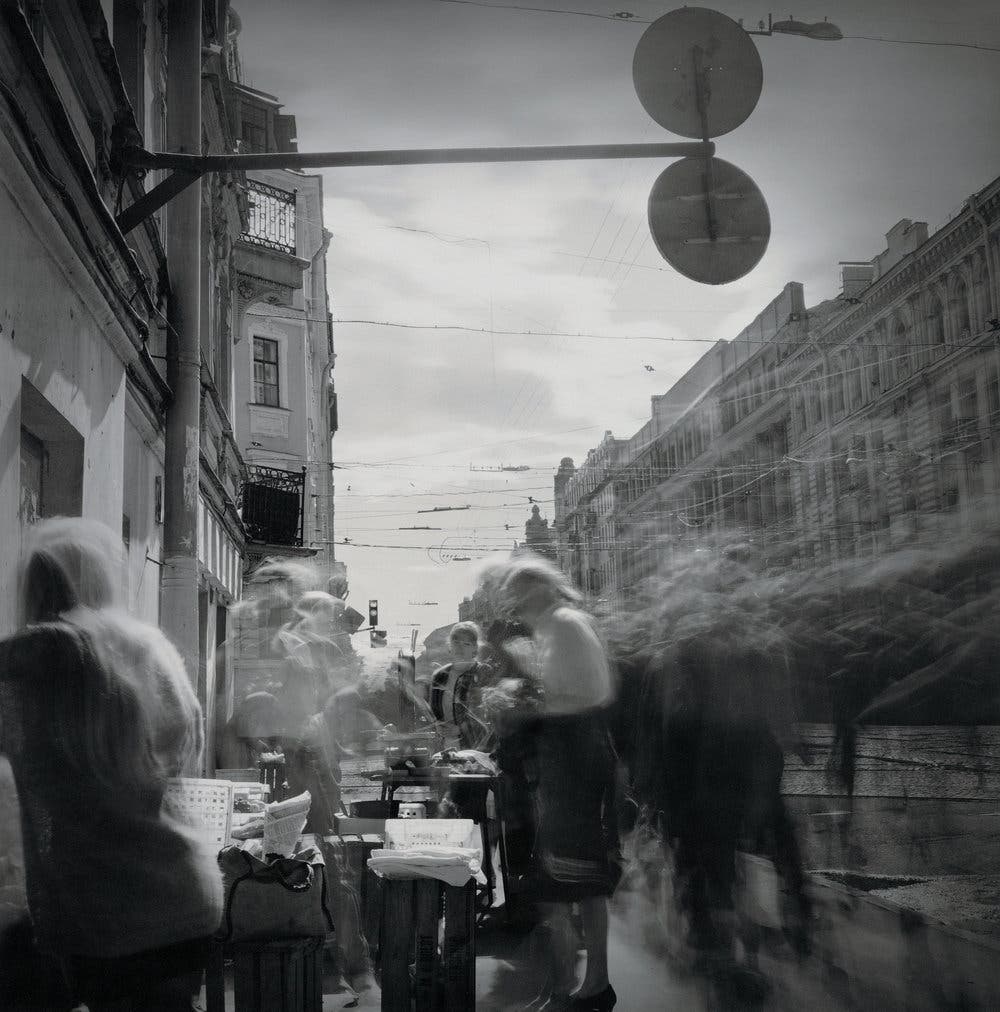 Old timey black and white photo showing a buzz of people in the city
