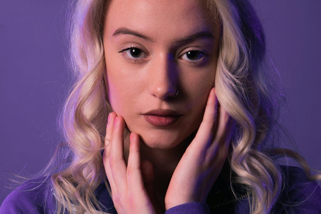 Blonde girl poses for a portrait with a purple background