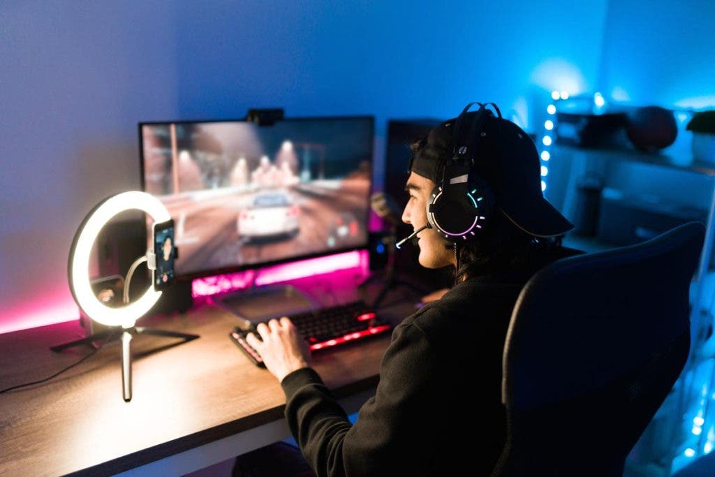 Latin young man laughing during a live stream on a smartphone. Handsome gamer feeling happy while playing a video game in his computer with neon led lights
