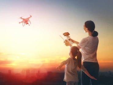 Little girl and her mother are operating the drone by remote control in the park. Kid and mom are playing with quadrocopter outdoors.