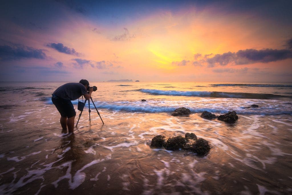Silhouette of a photographer with dramatic waves at sunrise. Landscape photography gear.