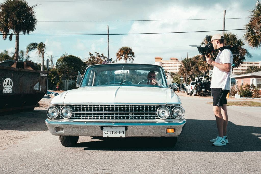 a man filming a movie outside of a vintage car