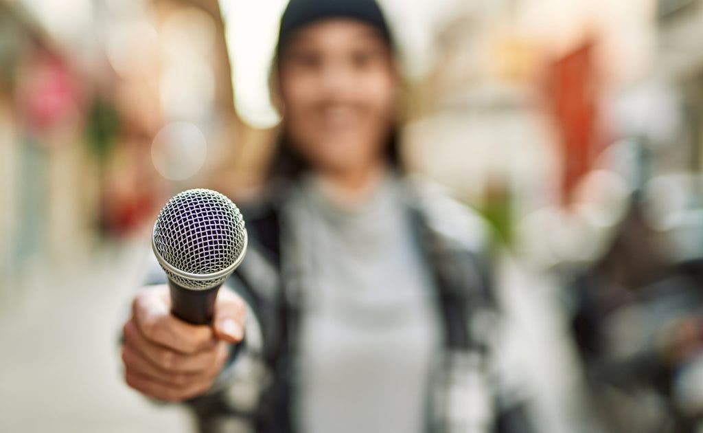 A young Hispanic woman smiling happily using the microphone in the city.