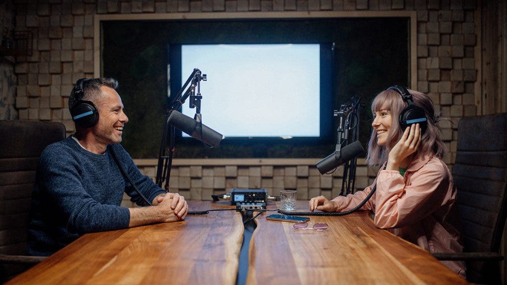 A young woman host talking into a microphone and interviewing a man for a radio podcast.