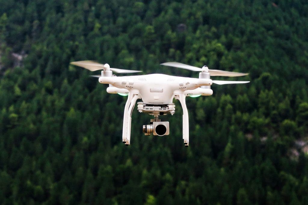 a white drone flying surrounded by greenery