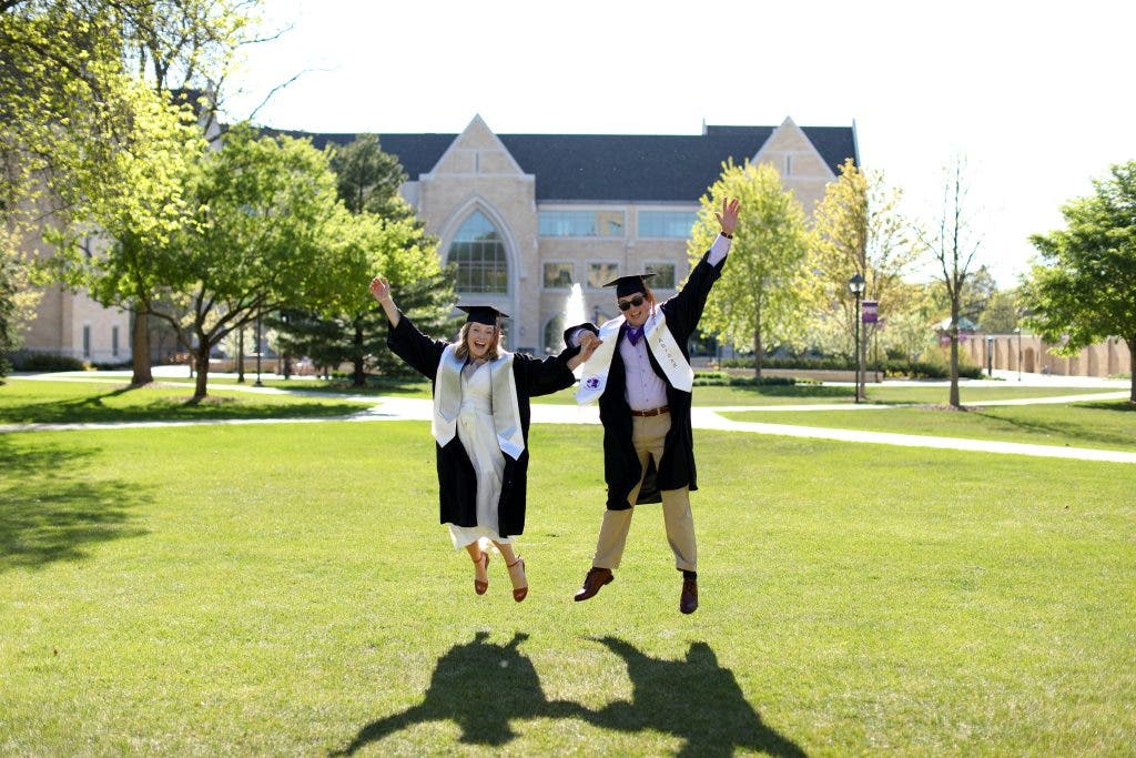 two fresh graduates taking a jump shot graduation photo