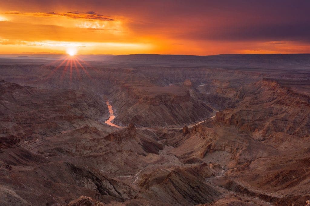 This photograph is of sunset over the immense and majestic Fish River Canyon, our subject. It conveys the monumental scale of the geological feature illuminated by the striking light of the setting sun. It has a few compositional anchors: